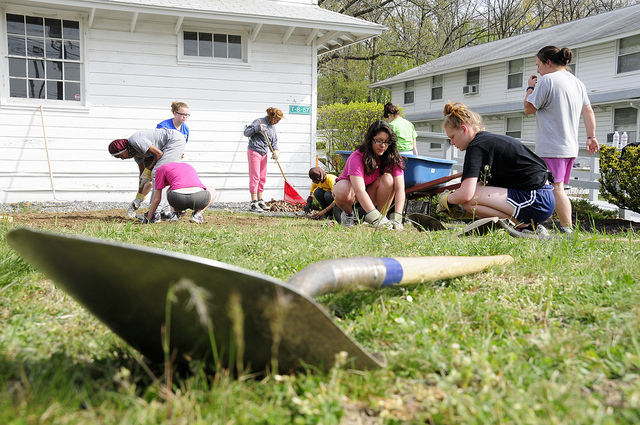 Young women who are Black and white, one wearing head covering, work on a garden