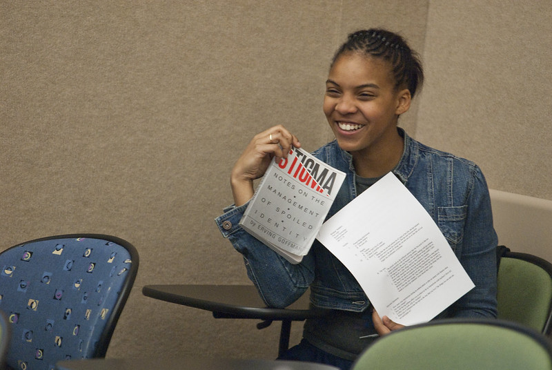 A Black girl smiles and holds Goffman's 'Stigma'