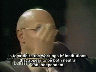 Foucault gestures emphatically with his hands and opens up his palm