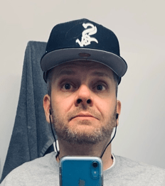 Benjamin Drury is a White man. He has a beard and is wearing earphones and a hat