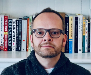 Headshot of Benjamin Drury. He is a White man with short hair and wears black glasses