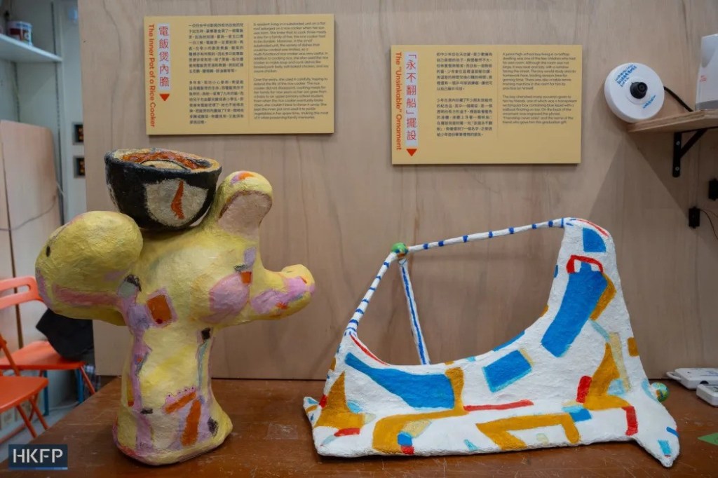 Artwork showing a three-arm, yellow sculpture next to a colourful bag