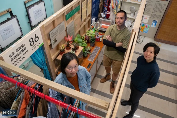 Aerial view of three people in a small, crowded space, beside plants and clothes.