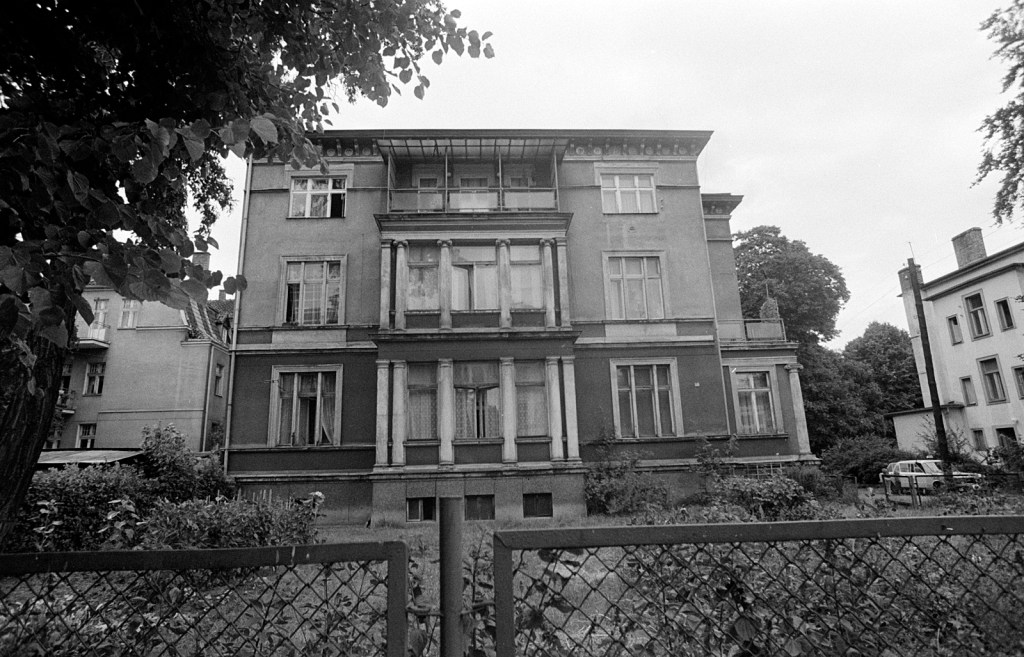 Black and white photo of a triple storey building in a surburban area behind a gate