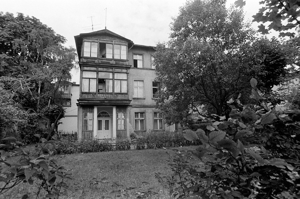 Black and white photo of a triple storey house in the background and a large garden with tall trees