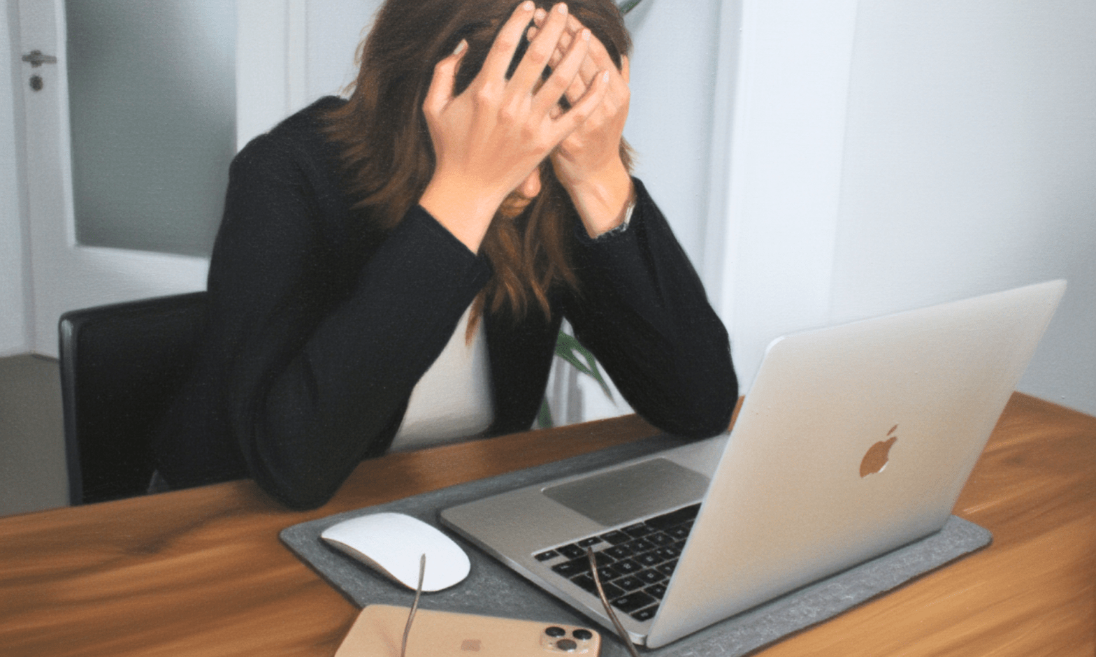 A white woman sits in front of a laptop, with her hands over her eyes