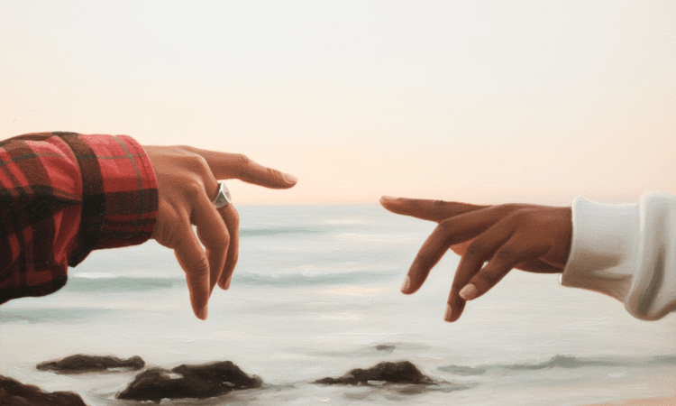 Close up of two Black people's hands reaching out to touch, with the sea in the background