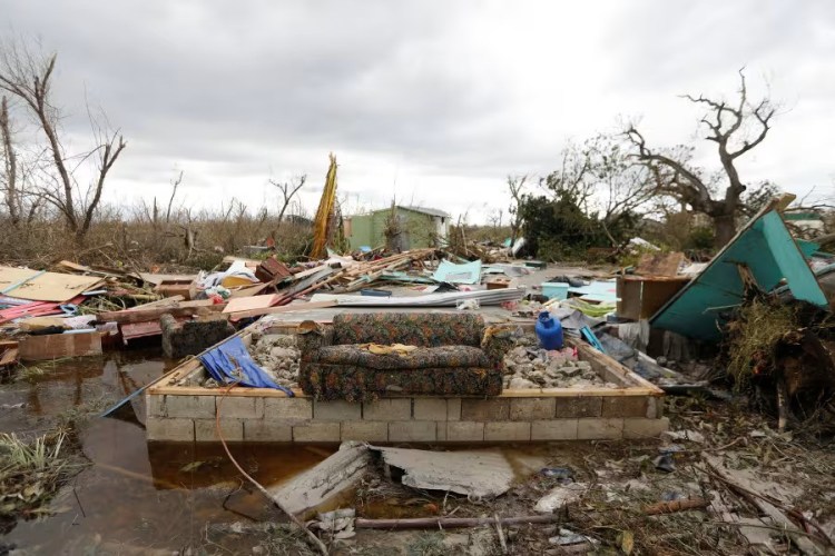 A ruined couch stands in the middle of debris, with broken wood and furniture in the background