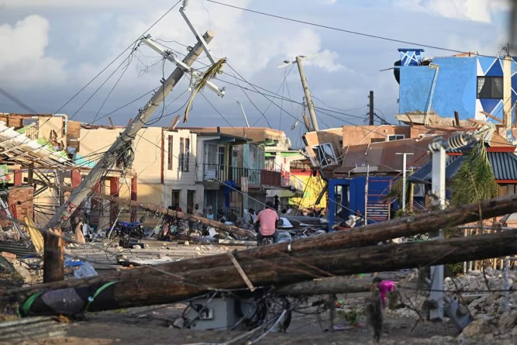 A Black man sits in the centre of fallen electricity poles with wood and rubble surrounding him
