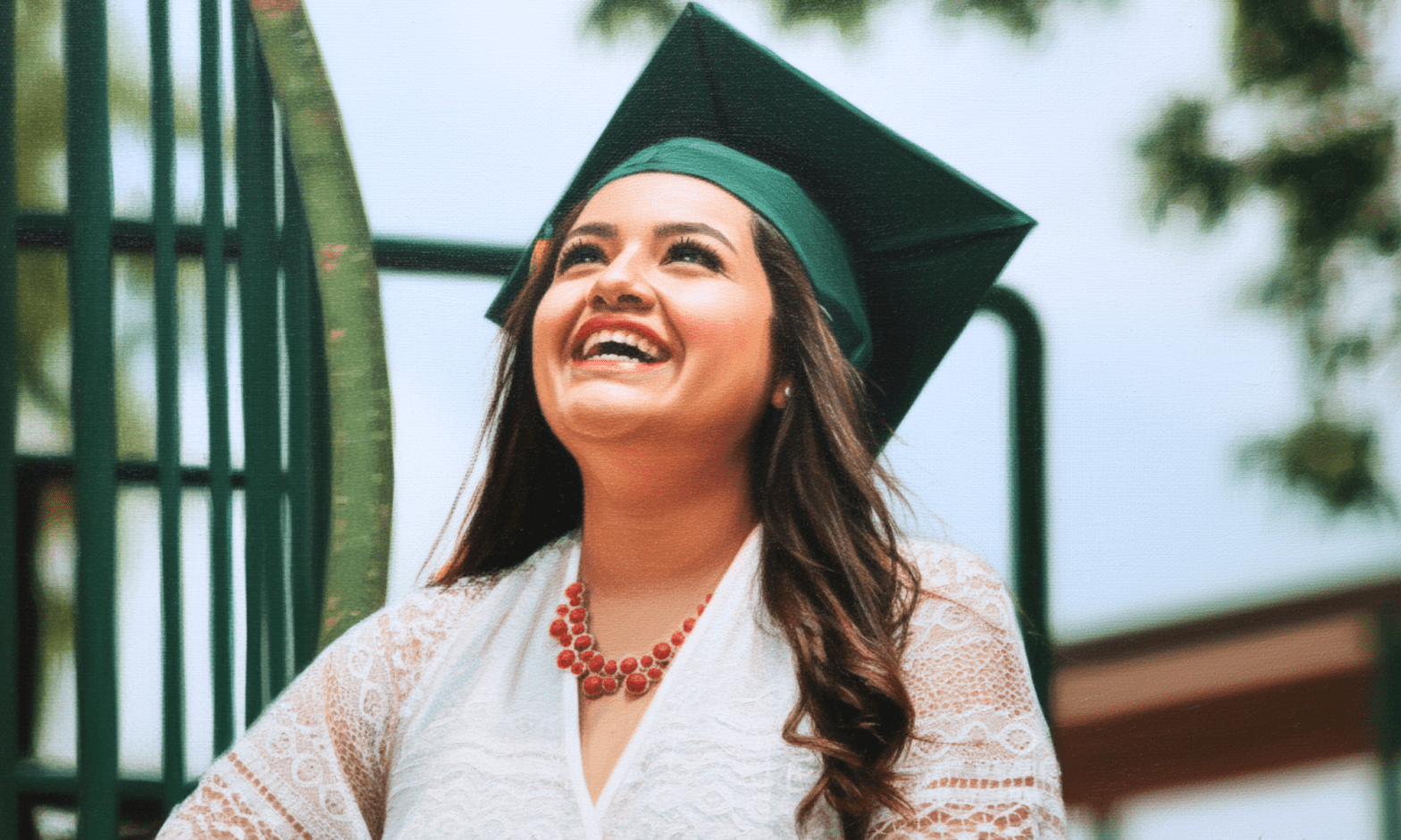 A Latina in a green graduation cap looks up, smiling
