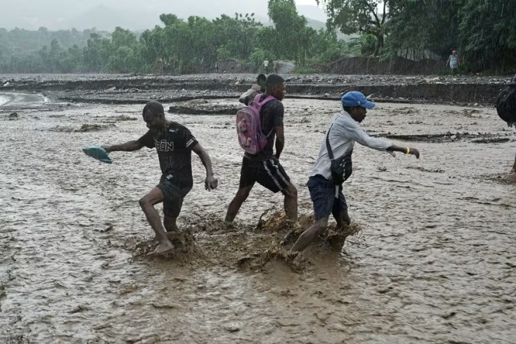 Three young men wade through muddy waters reaching their mid-calves in the rain