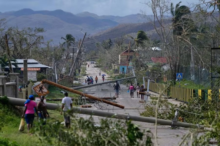 Black people walk into the distance, with fallen trees and telephone poles cluttering the road