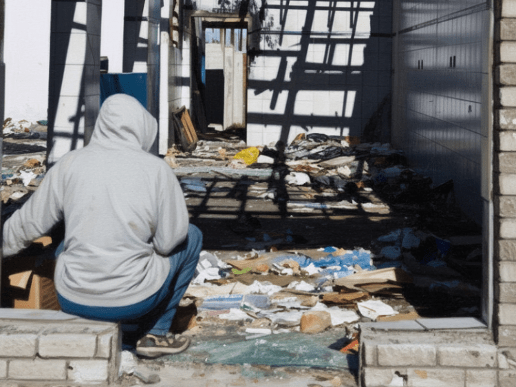 A person in a hoodie sits outside an unbuilt home