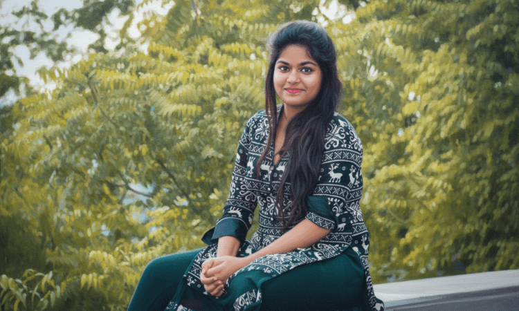 Indian woman sits outdoors with trees behind her. She is smiling softly and has long flowing hair