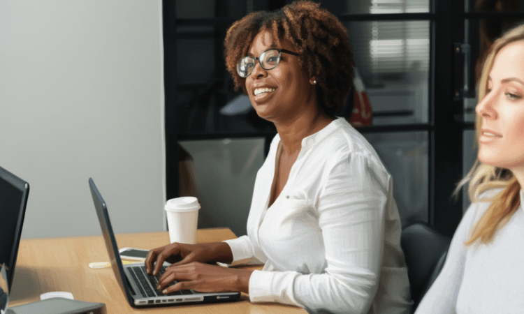 A Black woman with short, natural hair is looking up and smiling as she types on a laptop