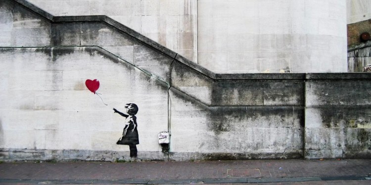 Street art of a girl reaching towards a heart-shaped balloon that's floating away