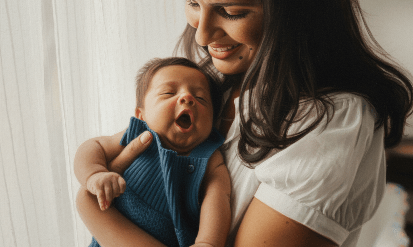 A brown woman smiles as she holds a yawning baby