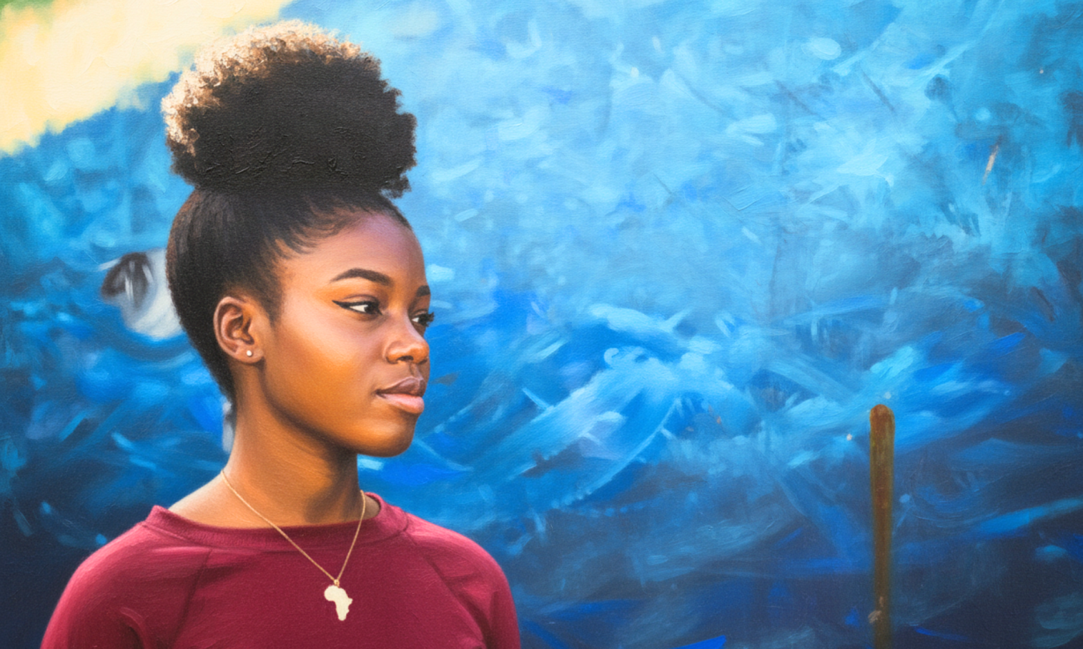 A Black girl wearing a pendant with the continent of Africa looks to the side, agaisnt an artistic mural