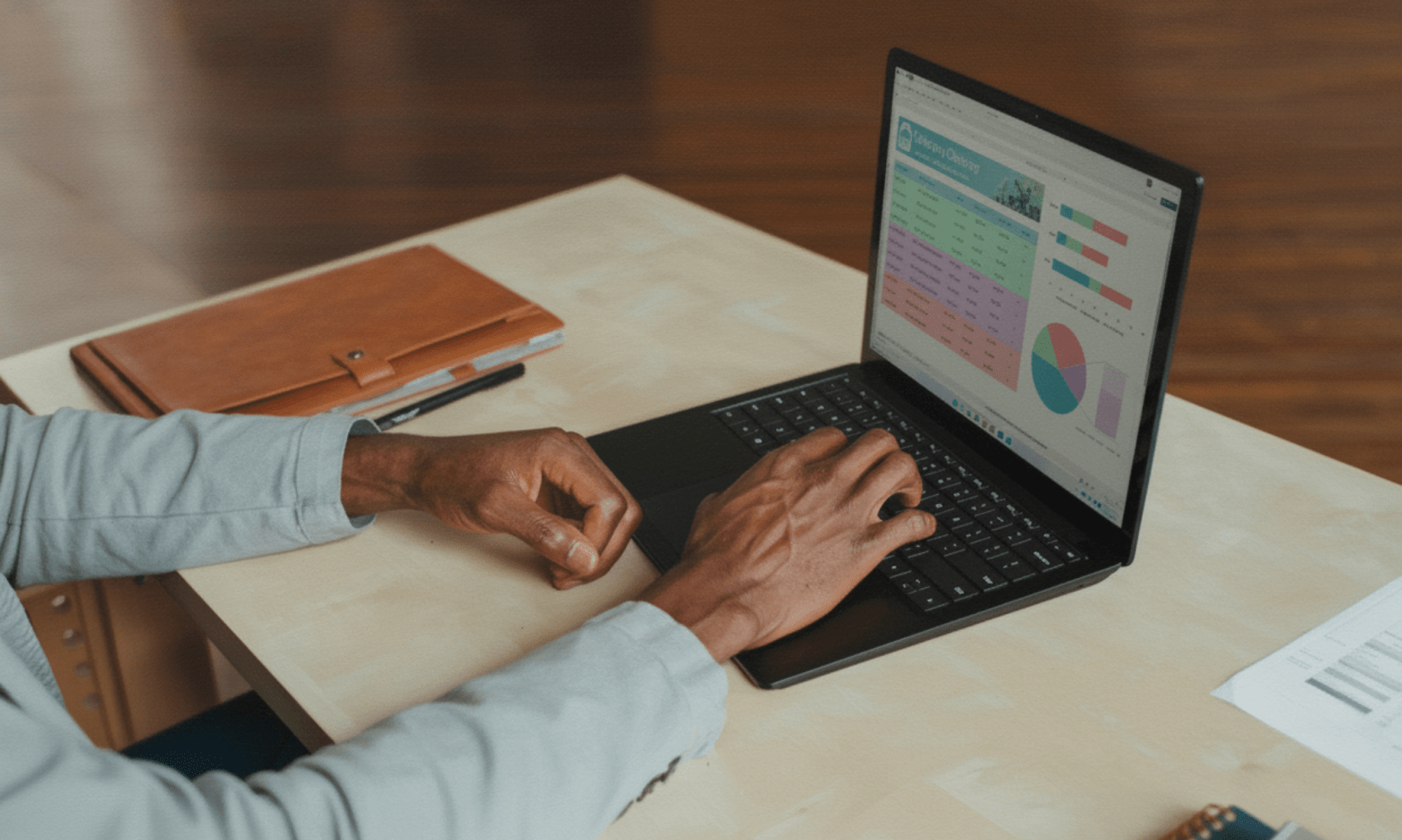 A Black man's hands and arms are seen from the side, as he writes on a laptop showing graphs