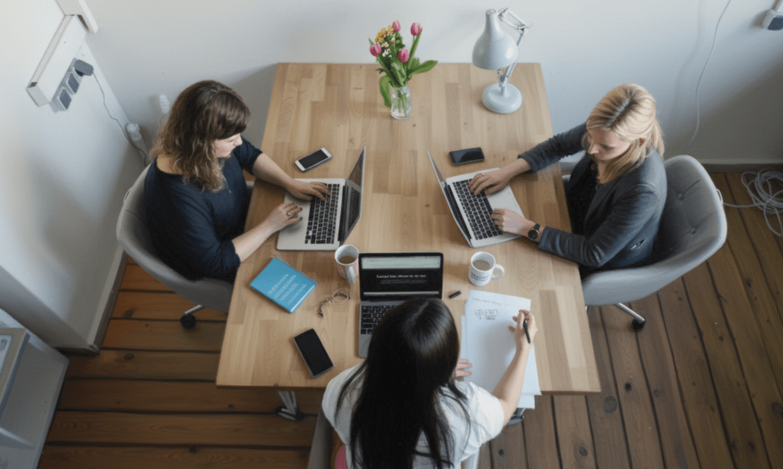 Aerial view of three white women working on laptops in a small meeting room