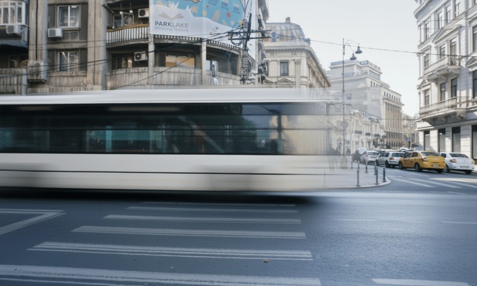 A large white bus in Bucharest, Romania, drives past in a whirl and large buildings are in the background. The street in the foreground are empty, and one man looks transparent and diminutive in the background