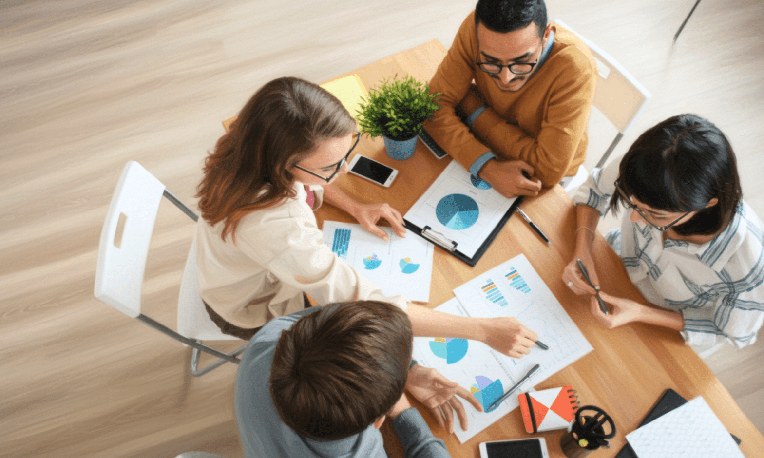 Aerial view of two men and two women seated around a table, as they point to graphs and charts