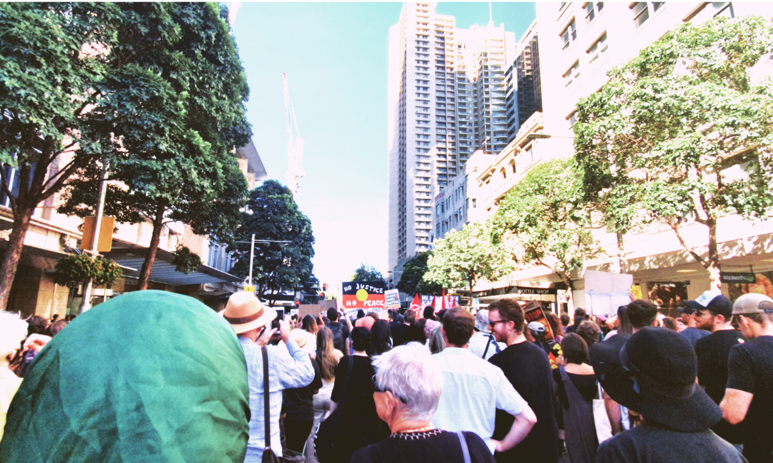 People protesting in Sydney, Australia, holding banners. One sign says, "No justice no peace," over the Aboriginal flag.
