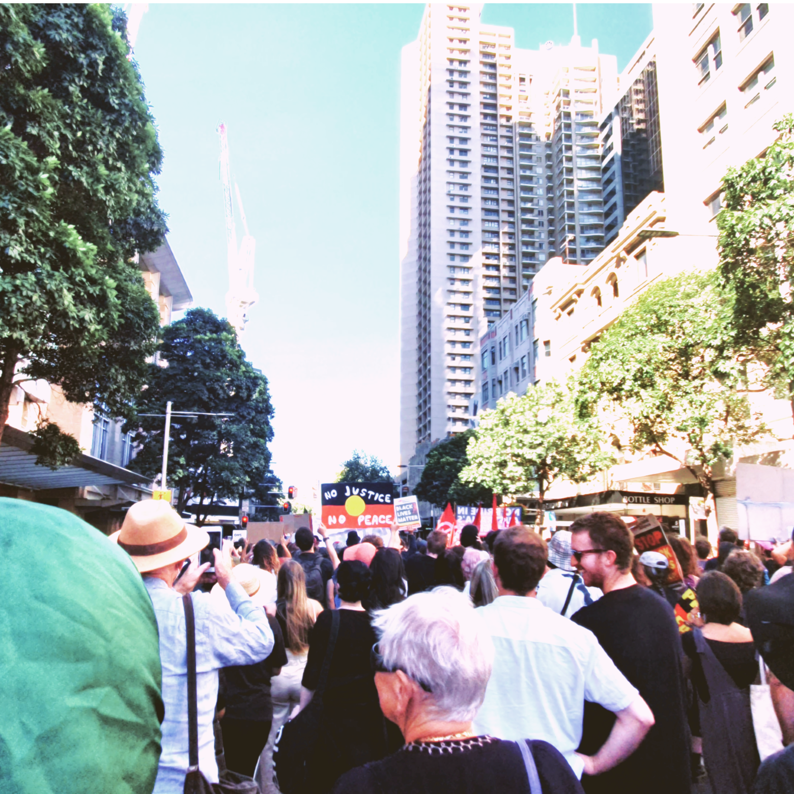 People protesting in Sydney, Australia, holding banners. One sign says, "No justice no peace," over the Aboriginal flag.