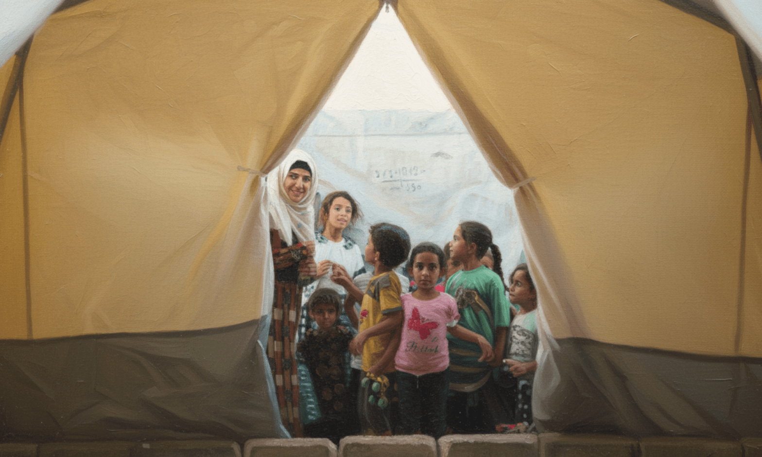Half a dozen children crowd around the entrance to a refugee tent, smiling and looking curious